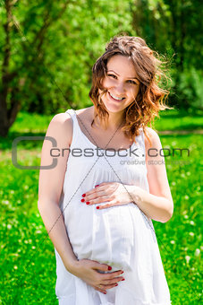 Woman holding her hands belly, waiting for the child on the park