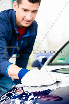 Hard-working man polishing car with white microfiber mitt