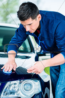 Happy man looking at camera while waxing a blue car