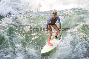 Atractive sporty girl surfing on famous artificial river wave in Englischer garten, Munich, Germany.