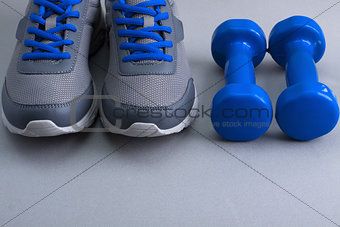 Sport equipment - sneakers and dumbbells on gray background.