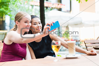 Young fashionable woman taking selfie with phone in cafe