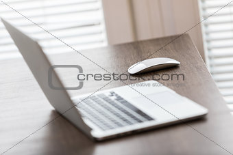 Laptop and cordless mouse on wooden desk