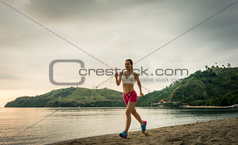 Fit young woman running on the beach during summer vacation in F