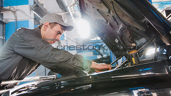 Mechanic male in automobile garage checking hood of the car for luxury SUV