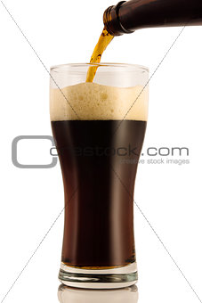 Dark beer poured into a glass from a bottle, isolated on a white background