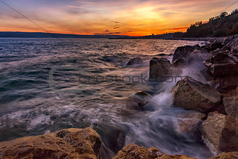 Sunset over the sea with splash waves on the rocks