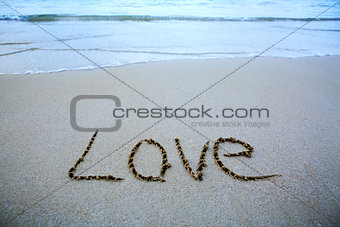 Word Love written on the sand near the sea.