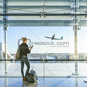 Young woman waiting at airport, looking through the gate window.