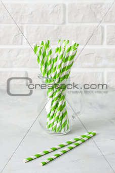 Glass jug with striped green drinking straws brick wall backgrou
