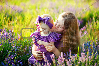 Mother hugs her little daughter in the rays of the setting sun, wearing long lilac dresses