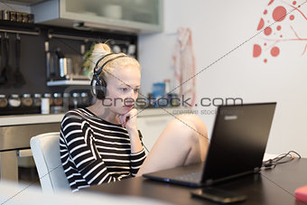 Adult woman in her casual home clothing working and studying remotely from her small flat late at night.