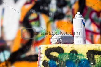 Two Discarded Spray Cans in Front of Graffiti Wall