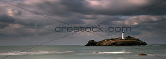 Stormy skies over Godrevy Lighthouse on Godrevy Island in St Ives Bay with the beach and rocks in foreground, Cornwall UK