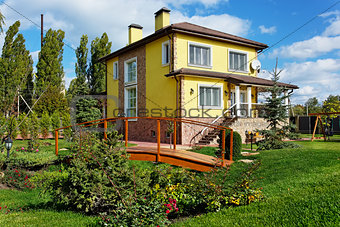 Exterior of luxury home with green yard and wooden bridge 