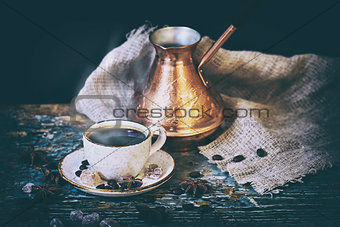 Cup of coffee and turkish coffee pot with coffee beans lying on a shabby wooden table