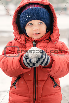 Sweet child in the snow with a snowball in his hands\