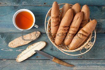 Mini baguettes in a basket on a wooden table, tea and a sandwich