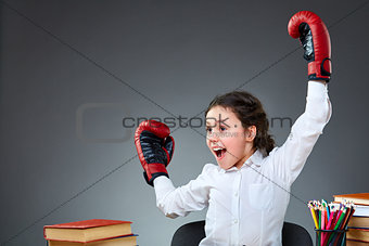 Playful cute little girl having fun in boxing gloves while leaning on grey background, selective focus