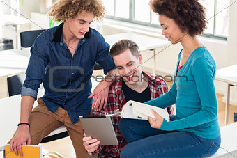 Three young students using both a book and a tablet PC for checking information