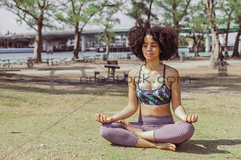 Content woman meditating in sunlight in park