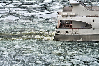 Ship sailing along icy river in early spring