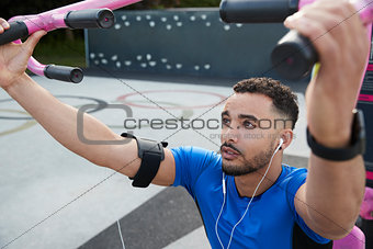 Young male athlete using outdoor gym in park, close up