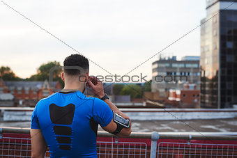 Male runner adjusting earphones in urban setting, back view