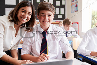Portrait Of Teacher Helping Pupil Using Computer In Classroom