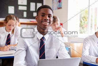 Portrait Of Male Pupil In Uniform Using Laptop In Classroom