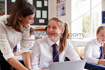 Female Teacher Helping Pupil Using Computer In Classroom