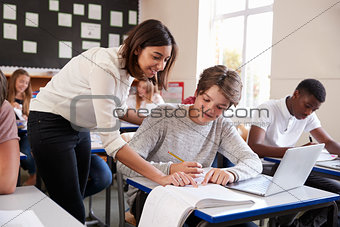 Teacher Helping Male Pupil Using Computer In Classroom