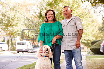 Portrait Of Senior Couple Walking Dog Along Suburban Street