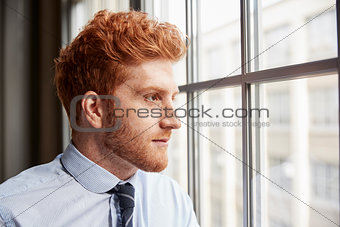 Young red haired bearded businessman looking out of window