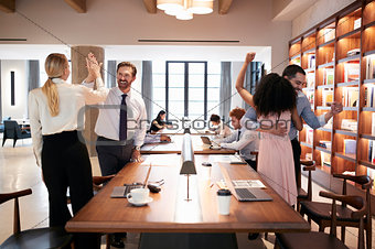 Four colleagues celebrating success in an open plan office