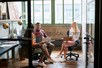 Three coworkers in a team meeting, seen through open door