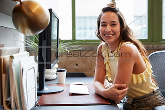 White woman at a computer in an office smiling to camera