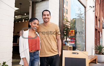 Young Hispanic couple smiling to camera outside their shop
