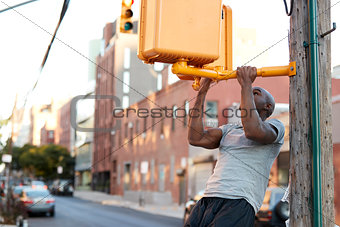 Young black man doing chin ups from crossing light in street