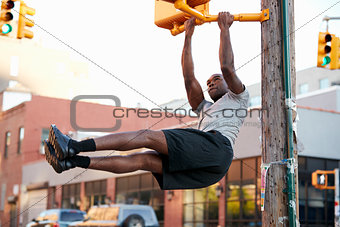 Young black man doing pull ups from crossing light in street
