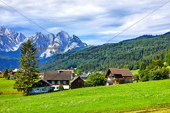 Austrian village among green meadows and Alps