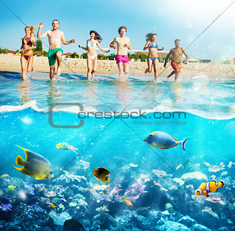 Group of friends run to the sea with colorful fishes. Concept of summertime