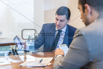 Two young businessmen using electronic devices at business meeting.