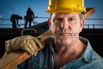 Serious Contractor in Hard Hat Carrying Wood Plank At Constructi