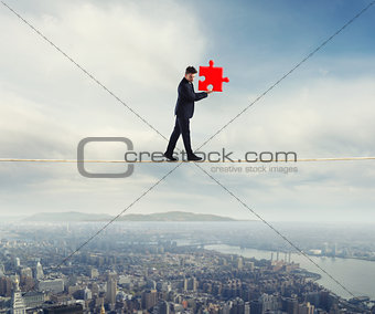 Businessman carries a piece of puzzle while he walking on a rope. concept of missing piece