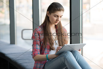 Portrait of Attractive Woman Working on Tablet near Big Window.