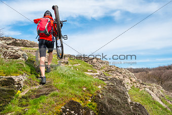 Enduro Cyclist Taking his Mountain Bike up to Beautiful Rocky Trail. Extreme Sport and Adventure Concept.