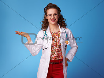 smiling pediatrist woman showing something on empty palm on blue