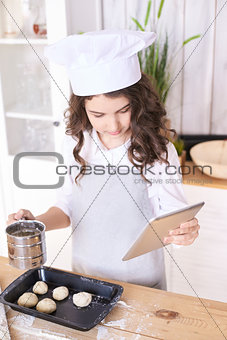Cooking buns. Girl with tablet in kitchen. Light wooden backgrou