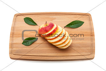 Sliced delicious luscious apple with green leaves on a cutting board made of wood.